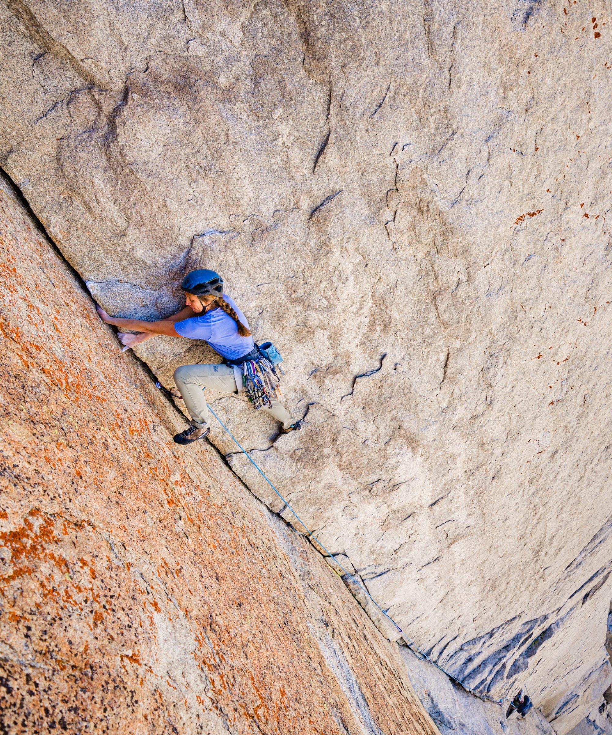 Chalky hands in the jam, a climber on a big wall pushes off the toe of her right foot, reaching her left out for a step up.