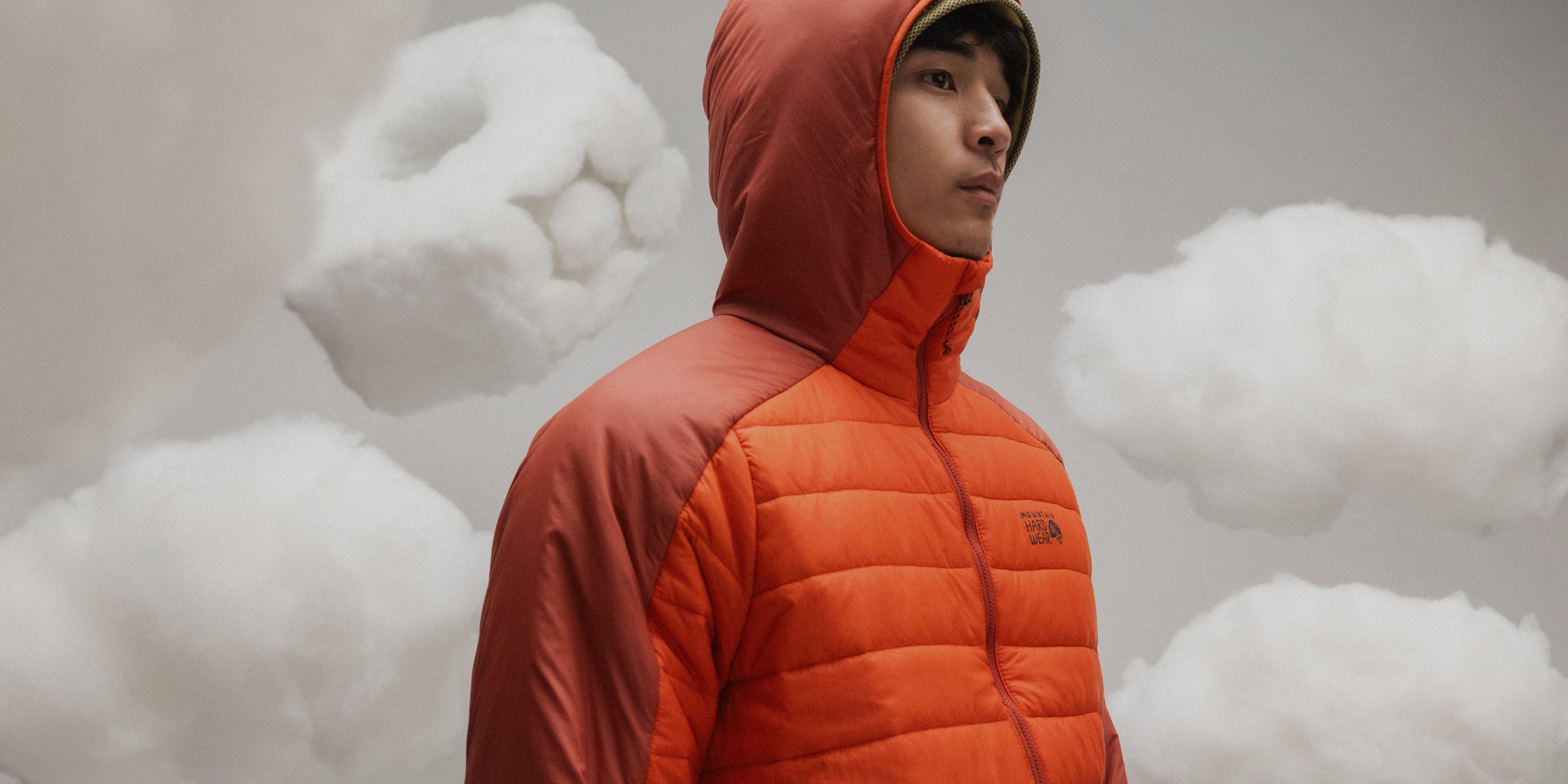 A model wearing the Free Element down jacket with fluffly clouds in the background, one being shaped like the Mountain Hardwear logo.