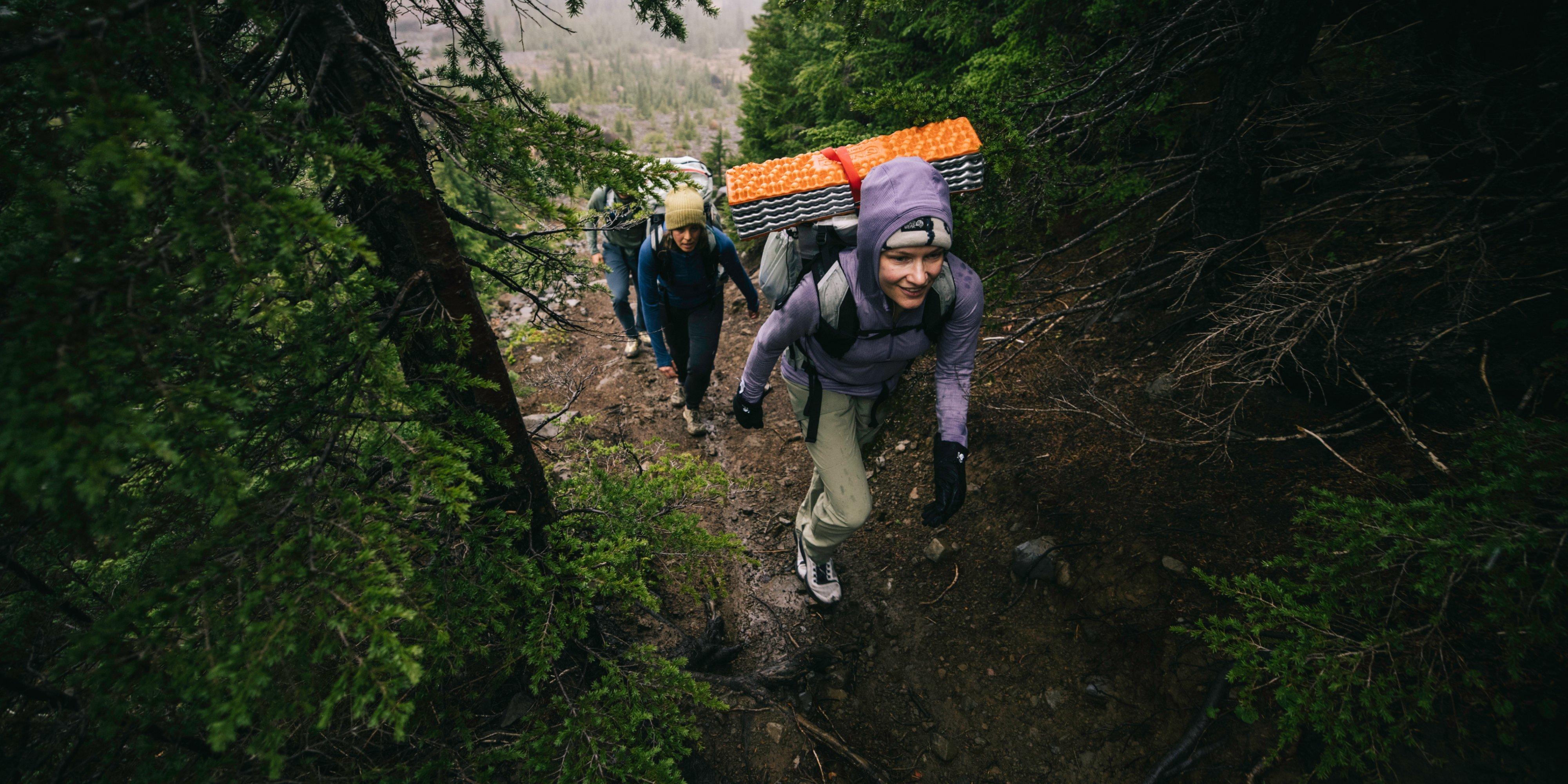 Wearing Kor Alloy™ Hooded Jackets and loaded Alakazam™ Backpacks, a trio ascends the muddy trail into the trees.