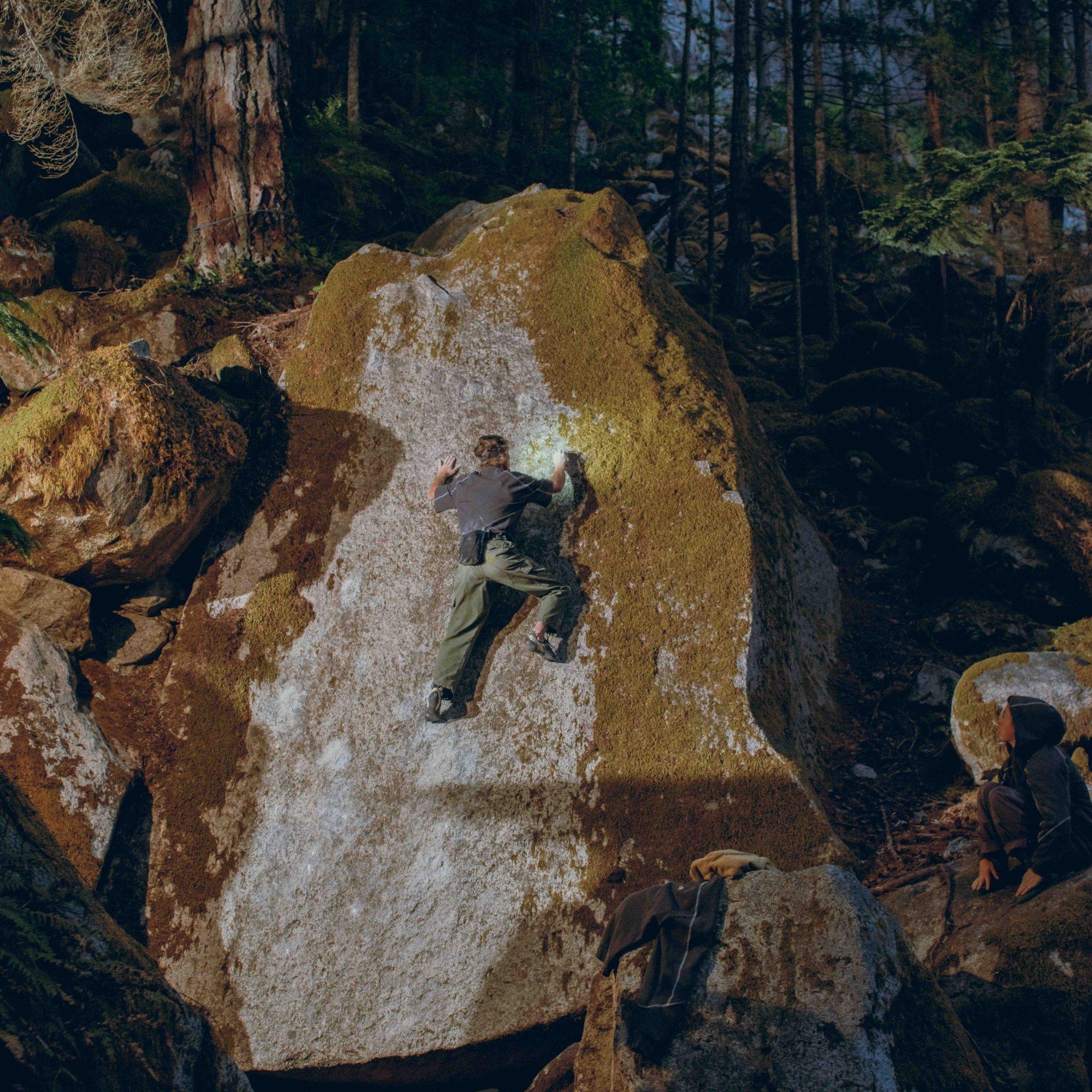Framed by shadowy trees, MHW Athlete Rell Lennox reaches for her chalk while bouldering, her headlamp illuminating her next move.