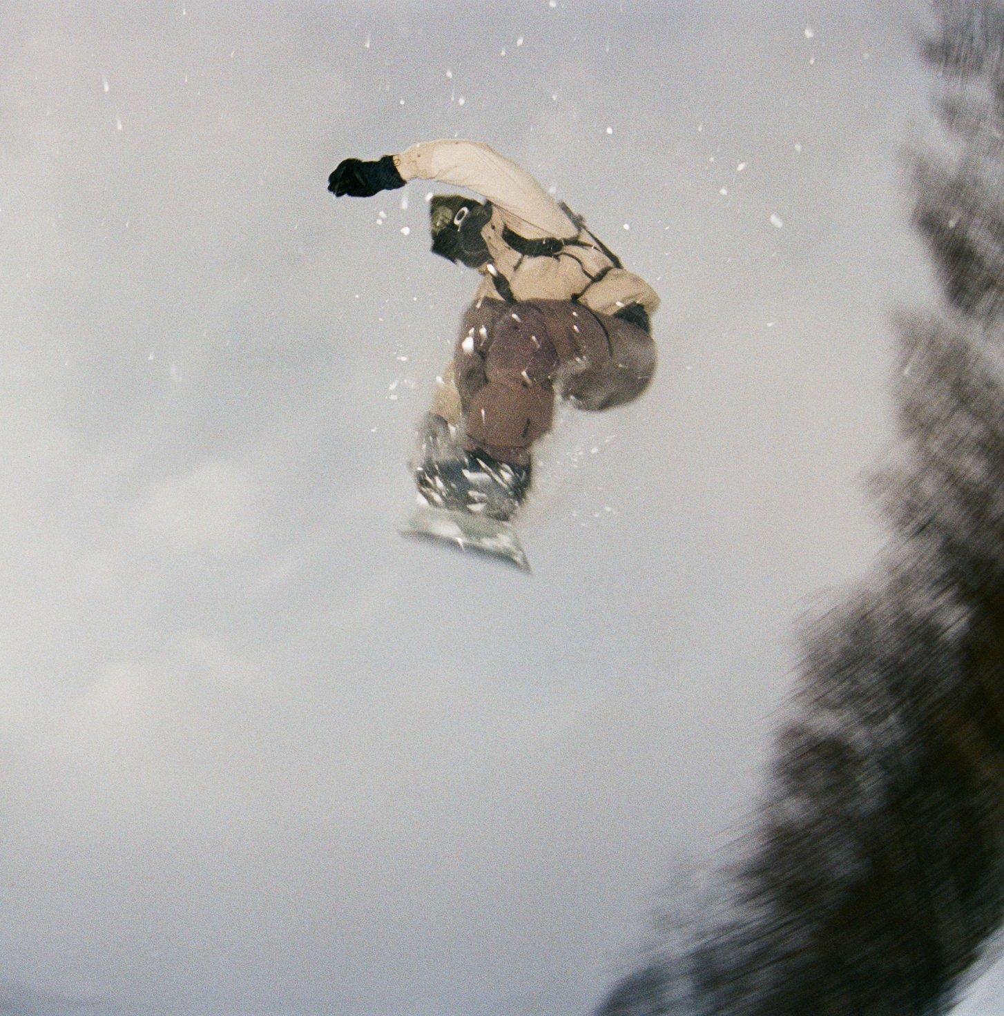 Snow flying as he sails along, a snowboarder pulls a mid-air indy grab.