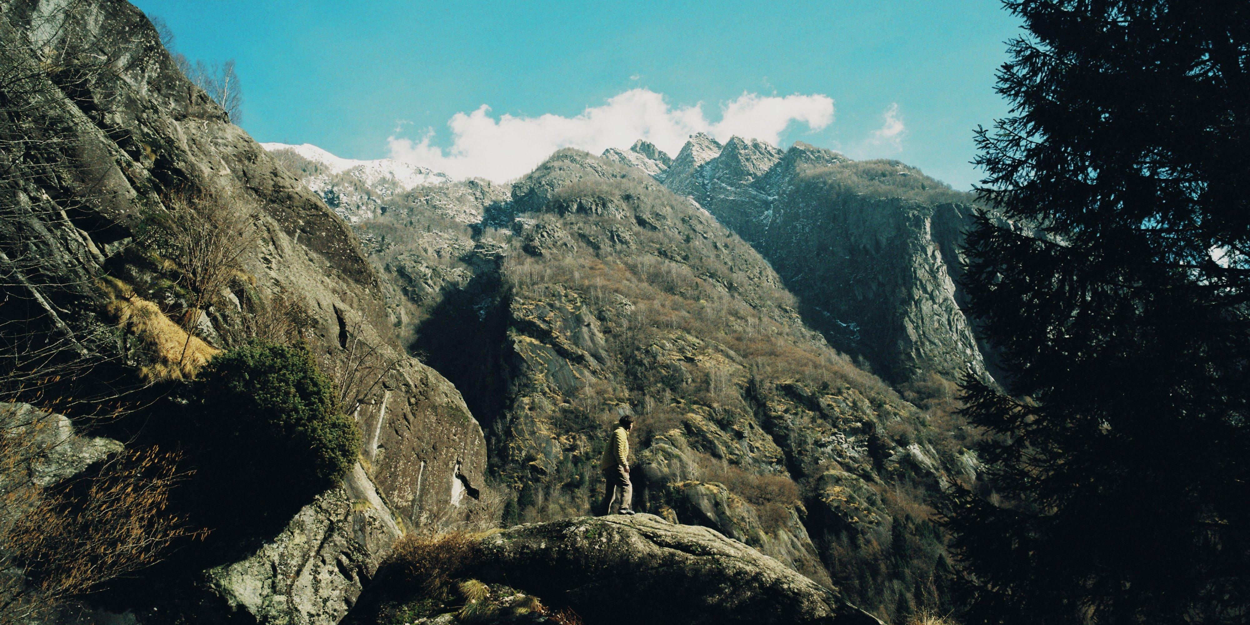 A climber in a StretchDown™ Jacket takes in the view from atop a large boulder surrounded by barren trees.