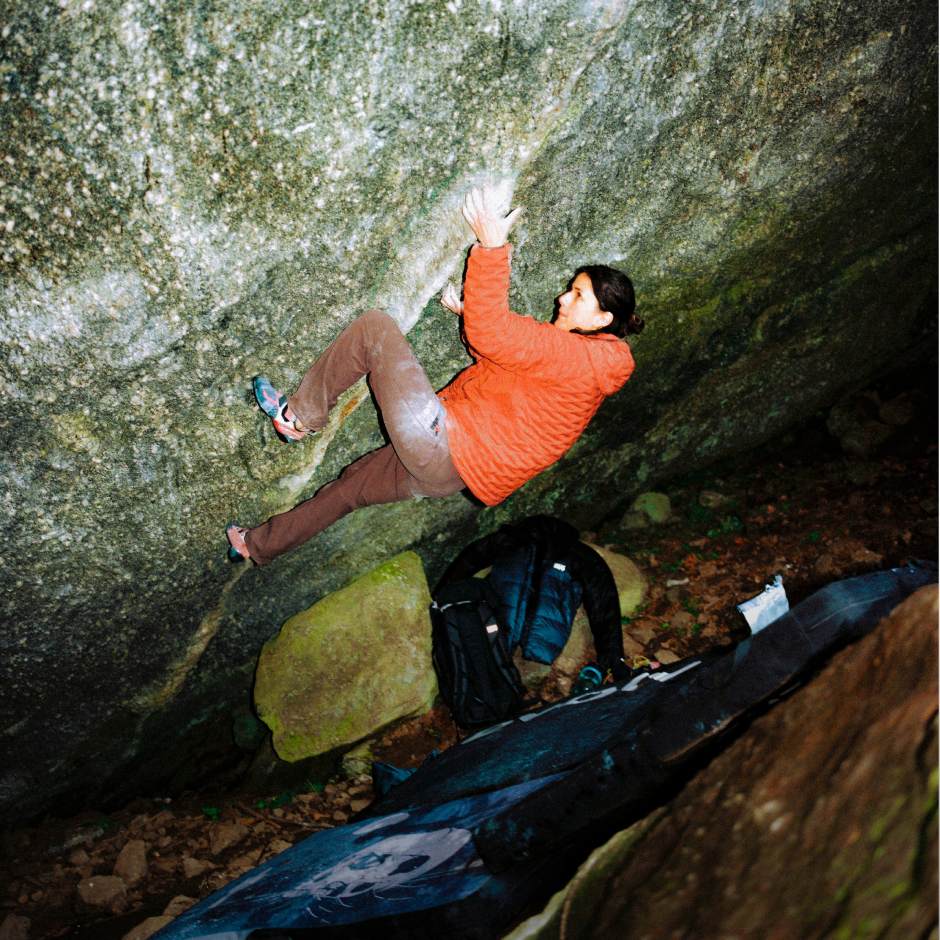 As night creeps in, a woman boulders in a StretchDown™ Hooded Jacket. On screen text reads: StretchDown™