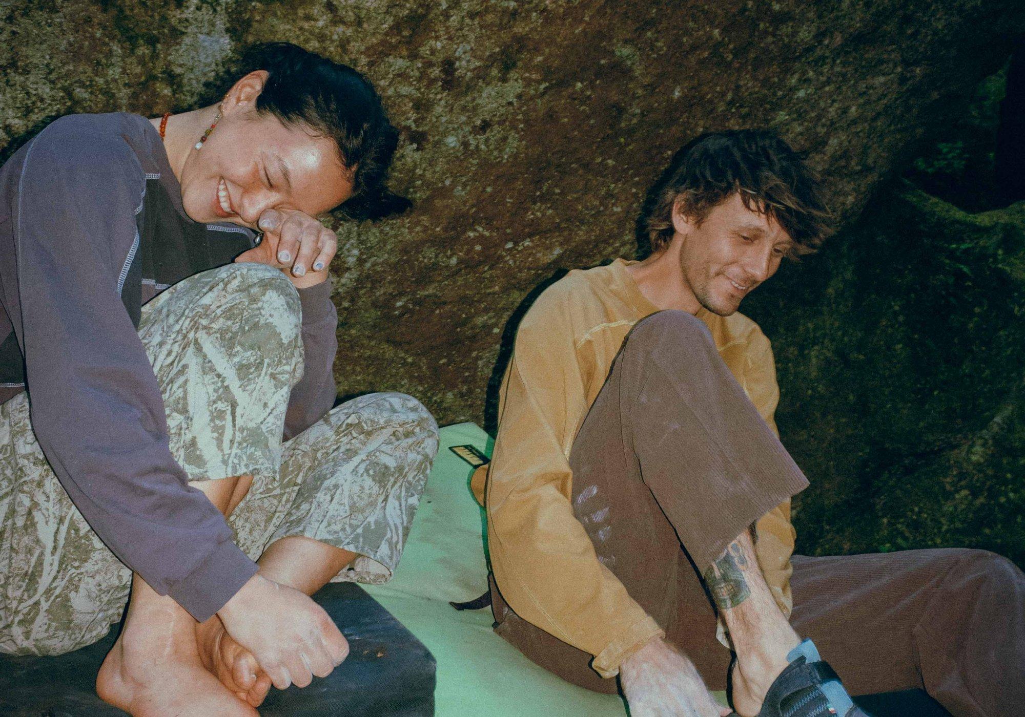 Seated on crash pads in chalk handprint-laden Rockrydge™ Pants, two climbers share an end-of-day laugh.